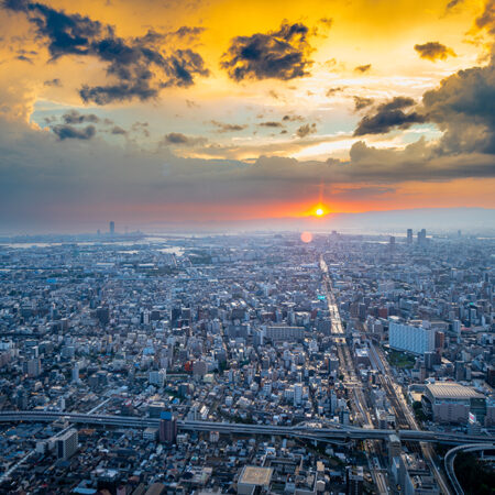 This is a stunning photo of an Osaka sunset displaying the skyline after a rain storm. The sky is ablaze with color, from the deep red of the sunset to the bright yellow and orange of the clouds. The city lights reflect off the wet streets, creating a magical scene. This photo is perfect for anyone who loves beautiful sunsets, city skylines, in Japan.